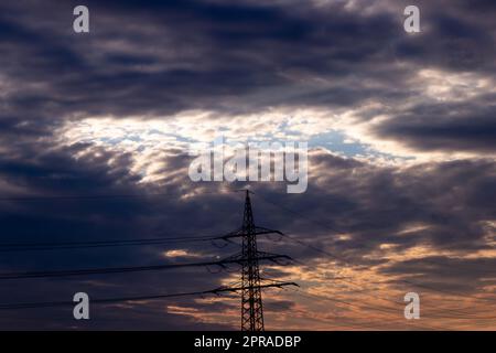 Le ciel doré aux rayons du soleil et à la lentille diffuse de l'énergie solaire avec une silhouette de pylône de tour d'électricité au coucher du soleil doré et un ciel orange pour une énergie durable ou des ressources renouvelables du crépuscule au soleil de l'aube Banque D'Images