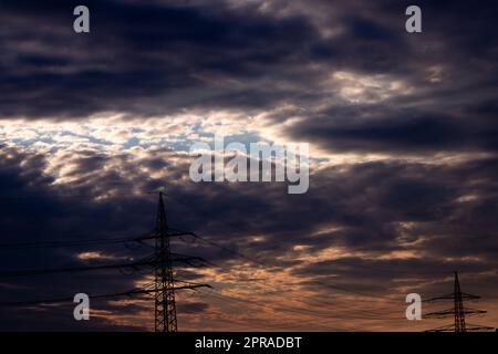 Le ciel doré aux rayons du soleil et à la lentille diffuse de l'énergie solaire avec une silhouette de pylône de tour d'électricité au coucher du soleil doré et un ciel orange pour une énergie durable ou des ressources renouvelables du crépuscule au soleil de l'aube Banque D'Images