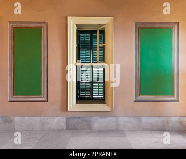 Fenêtre en bois avec volets verts médiant d'élégants cadres rectangulaires verts sur le mur orange Banque D'Images