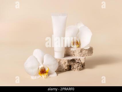 Tube blanc crème près de la fleur blanche d'orchidée sur jaune clair, maquette. Produit de soin de la peau Banque D'Images