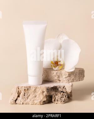 Tube blanc crème près de la fleur blanche d'orchidée sur jaune clair, maquette. Produit de soin de la peau Banque D'Images