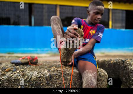 Un jeune joueur de football afro-colombien enlève ses crampons après une session d'entraînement sur un terrain de jeu de terre à Quibdó, Chocó, Colombie. Banque D'Images