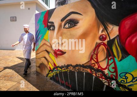 Un serveur marche autour d'un coin à Málaga, Espagne; murale d'une femme espagnole portant des boucles d'oreilles Banque D'Images