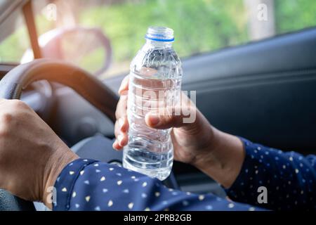 Femme asiatique chauffeur tenant une bouteille pour boire de l'eau tout en conduisant une voiture.Une bouteille d'eau chaude en plastique peut provoquer un incendie. Banque D'Images