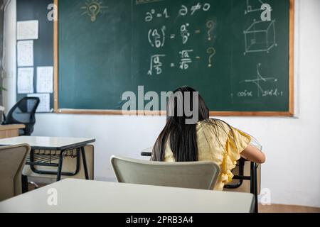 Vue arrière de l'école fille sur la leçon en classe écrire dur sur le tableau noir Banque D'Images