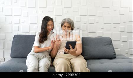 La jeune femme asiatique et sa grand-mère agitant la main par la communication à distance via un ordinateur tablette dans le salon. Famille heureuse vivant ensemble Banque D'Images