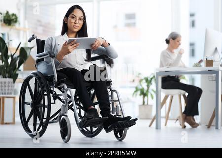 Axé sur la réussite. Portrait complet d'une jeune femme d'affaires attirante en fauteuil roulant utilisant sa tablette au bureau. Banque D'Images