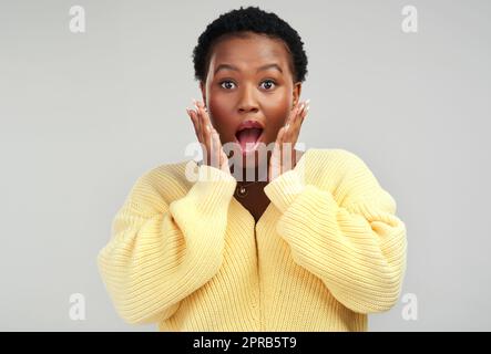 Le secret est sorti: Une jeune femme qui a l'air surpris en posant sur un fond gris. Banque D'Images