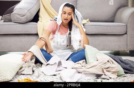 Les vêtements jetables devraient être une chose. Une jeune femme se sentant submergée tout en s'asseyant dans un salon désordonné. Banque D'Images