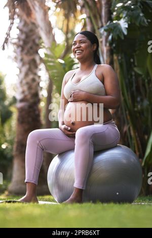 Mon bébé est aussi actif que moi. Une femme enceinte assise sur un ballon de stabilité à l'extérieur. Banque D'Images