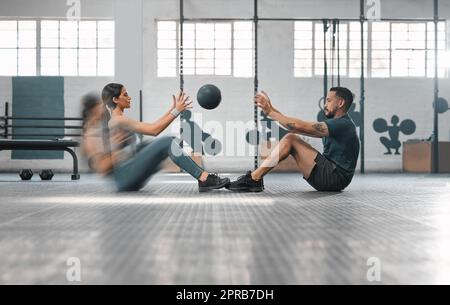 Un couple sportif actif ou un partenaire sportif s'entraîne ensemble, faisant des exercices d'abs en lançant une balle lestée. Entraîneur masculin et athlète féminine en mouvement se sont concentrés sur la séance d'entraînement ou la classe. Banque D'Images