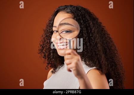 I À plus. Portrait court d'une jeune femme attrayante regardant à travers une loupe en studio sur fond rouge. Banque D'Images