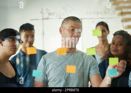 Travail d'équipe, planification et rédaction de notes autocollantes tout en remue-méninges, en parlant et en partageant des idées. Responsable dirigeant un groupe diversifié de personnes d'affaires créatives en réunion tout en faisant preuve de vision et d'innovation Banque D'Images