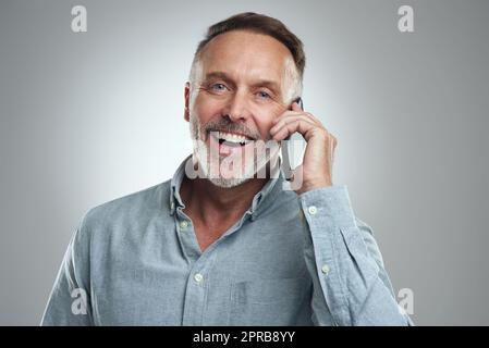 C'est juste la nouvelle que je voulais entendre. Portrait studio d'un homme mûr parlant sur un téléphone portable sur fond gris. Banque D'Images