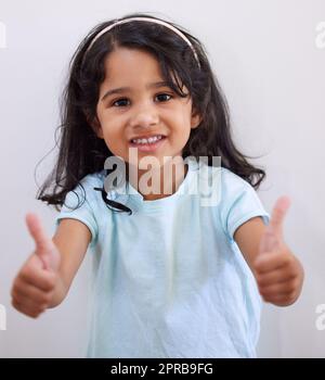 Êtes-vous bien. Une adorable petite fille montrant les pouces vers le haut tout en posant contre un mur. Banque D'Images