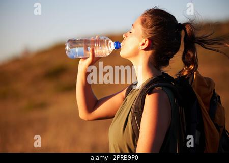 Vous ne vous ennuierez pas de la randonnée mais vous aurez soif. Une jeune femme boit de l'eau pendant une randonnée. Banque D'Images