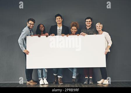 Groupe de professionnels tenant un tableau ou une affiche vierge avec un espace de copie sur fond gris. Divers espaces publicitaires d'équipe ou un poste vacant à leur démarrage. Des collègues souriants font de la publicité sur un écriteau Banque D'Images