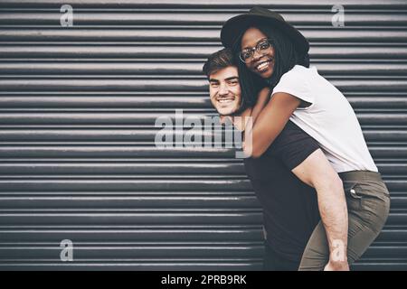 Couple interracial mignon, aimant et affectueux, amusant, ludique et amusant, sur fond d'espace de copie. Un petit ami heureux donnant à une petite amie une promenade en pigeyback à l'extérieur Banque D'Images