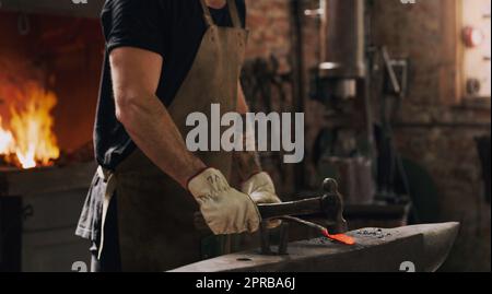 Je peux le transformer en presque tout. Un ouvrier en métal frappant une tige en métal chaude avec un marteau dans un atelier de soudage. Banque D'Images