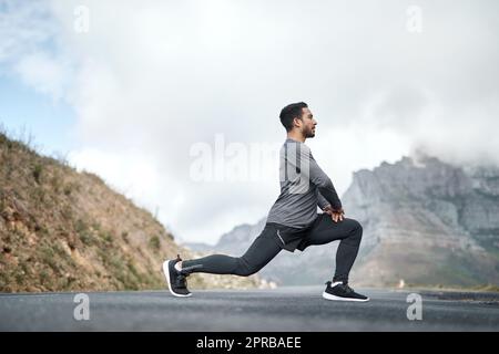 Je prends le temps d’étirer mes jambes avant de faire de l’exercice. Prise de vue en longueur d'un beau jeune homme qui s'étire avant de faire de l'exercice à l'extérieur seul. Banque D'Images