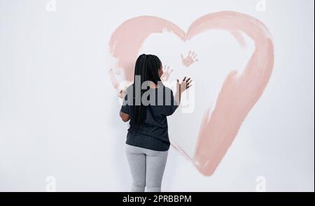 Au lieu d'une carte de Saint-Valentin, pourquoi ne pas parler d'une fresque. Une jeune femme peint un coeur sur un mur. Banque D'Images