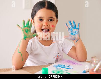 C'est tellement amusant. Une adorable petite fille assise à la maison avec de la peinture à base d'eau enduite ses mains. Banque D'Images