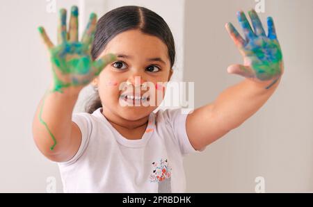 Qui a besoin de papier. Une adorable petite fille assise à la maison avec de l'eau à base de peinture étalé sur ses mains. Banque D'Images