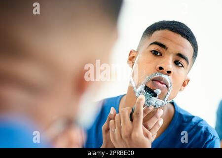 Il est temps d'être rasé de nouveau un moment de propreté. Un jeune homme concentré qui vérifie son reflet lorsqu'il se rase du visage. Banque D'Images