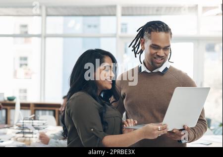 Tout semble se passer comme prévu : deux jeunes hommes d'affaires se tenant ensemble et utilisant un ordinateur portable au bureau. Banque D'Images