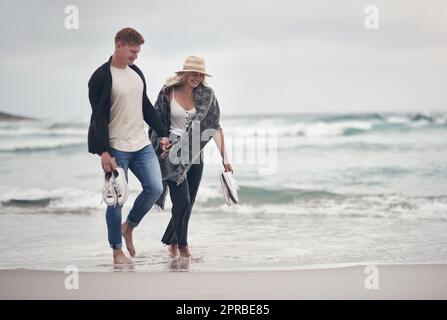 Nous adorons aller dans des endroits qui nous rapprochent les uns des autres. Un couple tient la main tout en se promenant sur la plage. Banque D'Images