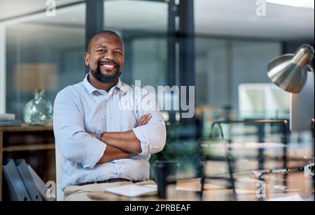 Travailler pour atteindre mes objectifs un quart de travail tardif à la fois. Portrait court d'un beau homme d'affaires mature assis seul dans son bureau la nuit avec ses bras pliés. Banque D'Images