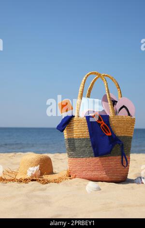 Sac avec accessoires de plage et chapeau sur sable près de la mer Banque D'Images