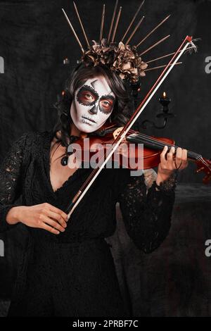 Musique d'ambiance pour Halloween. Portrait court d'une jeune femme attirante vêtue de son costume d'halloween de style mexicain jouant un violon. Banque D'Images