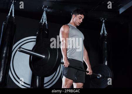 Construisez votre chemin vers un meilleur vous. Un jeune homme levant une barbell pendant son entraînement dans une salle de gym. Banque D'Images