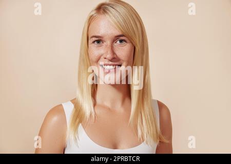 Portrait d'une belle femme avec des taches de rousseur en studio. Jeune femme avec une peau parfaite sur fond beige. Banque D'Images
