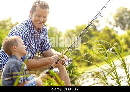 Les poissons sont sur leur chemin, fils. Père et fils assis ensemble à côté d'un lac avec leurs cannes à pêche. Banque D'Images