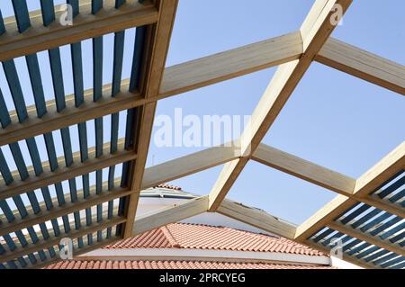 Un toit en bois est moderne du soleil avec des planches avec des poutres et des trous sur le fond d'un toit en tuiles avec des tuiles rouges contre le ciel bleu. Banque D'Images