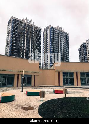 il y a un centre commercial rond beige dans la cour résidentielle. les bancs ronds lumineux sont destinés aux amateurs de shopping. derrière se trouvent les tenements en verre bleu pour le t Banque D'Images