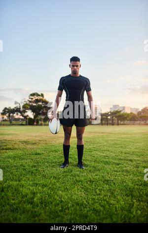 Mes objectifs sportifs sont écrasants. Portrait complet d'un jeune sportif charmant debout seul et tenant un ballon de rugby avant un entraînement matinal. Banque D'Images