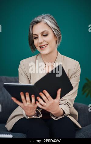 Rester au fait des tâches. Une femme d'affaires attirante et mûre assise seule et utilisant une tablette dans son bureau à domicile. Banque D'Images