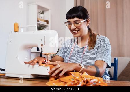 J'ai mon propre style donc je conçoivent mes propres vêtements. Une jeune femme qui coud du tissu à l'aide d'une machine à coudre à la maison. Banque D'Images