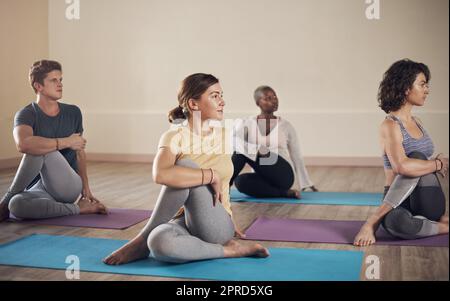 Relâchement de la tension de ma colonne vertébrale. Prise de vue en longueur d'un groupe diversifié de yogis tenant une posture de demi-torsion de la colonne vertébrale pendant une séance de yoga en intérieur. Banque D'Images