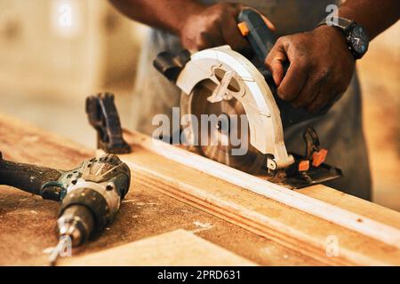 Nous allons couper. Un menuisier méconnaissable à l'aide d'une scie circulaire pour couper le bois à l'intérieur d'un atelier. Banque D'Images