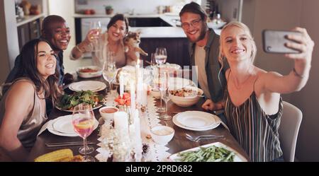 Ce ne serait pas la saison des fêtes sans de bons amis. Un groupe de jeunes amis prenant des selfies lors d'un dîner à la maison. Banque D'Images