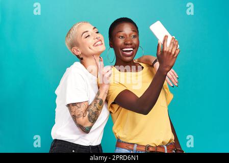 Les meilleurs amis font les meilleurs souvenirs. Photo en studio de deux jeunes femmes qui prennent des selfies ensemble sur fond turquoise. Banque D'Images