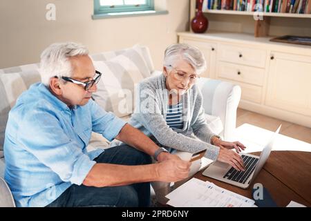 Régler leurs factures avec la commodité du crédit. Un couple senior utilisant une carte de crédit tout en passant par la paperasse à la maison. Banque D'Images