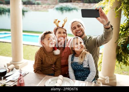 Joyeux Noël, de ma famille à la vôtre. Une famille de quatre personnes prenant un selfie ensemble le jour de Noël. Banque D'Images