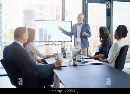 Le directeur des ventes fait une présentation sur la stratégie marketing et de la marque lors d'une réunion de conseil d'administration. Le responsable homme réussi, d'entreprise et mature pointe vers un graphique sur l'écran du moniteur pour montrer la planification Banque D'Images