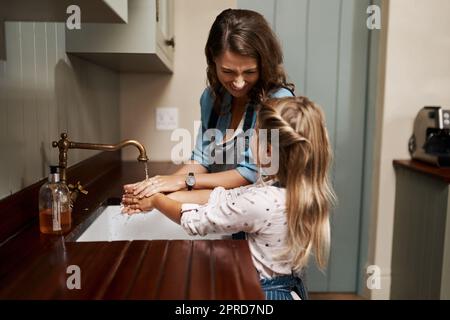 Mais tout d'abord, lavez-vous les mains. Une femme et sa jeune fille se lavent les mains dans la cuisine à la maison. Banque D'Images