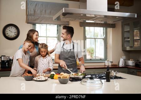 Nous adorons les week-ends parce que nous pouvons tout faire ensemble. Une jeune famille cuisine dans la cuisine. Banque D'Images